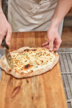 İtalyan mutfağı ve yemek pişirme konsepti. Napoli Pizzacısı 'nda pizza dilimleyen bir şef..