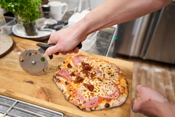 Italian kitchen and cooking concept. Chief with a pizza cutter cutting pizza to pieces at Neapolitan pizzeria.