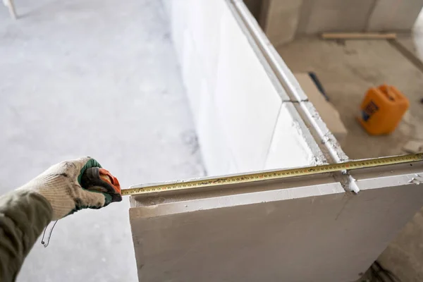 Працівник будівництва вимірює стрічкою міру Гіпсової пластини. Будівництво внутрішніх стін в квартирі з використанням гіпсової бетонної плити з канавками. гіпсові блоки язика і канавки — стокове фото