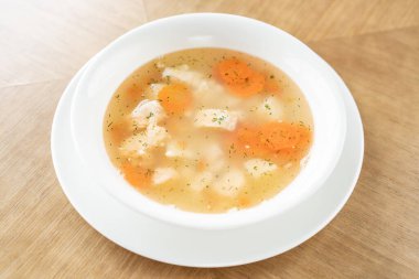 Fish soup in a white plate. Fish soup with vegetables, celery in a cup for the broth. Pike perch and salmon. Plate on wooden table. Restaurant menu