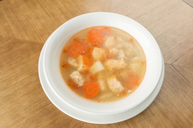 Fish soup in a white plate. Fish soup with vegetables, celery in a cup for the broth. Pike perch and salmon. Plate on wooden table. Restaurant menu