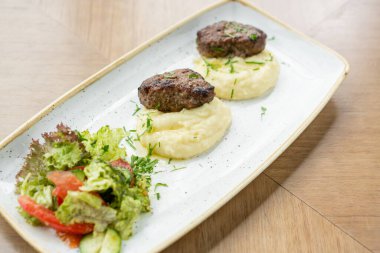 Lezzetli, sulu et pirzolası, yeşillik serpilmiş patates püresi ve taze sağlıklı domates salatası ve marul yaprakları..