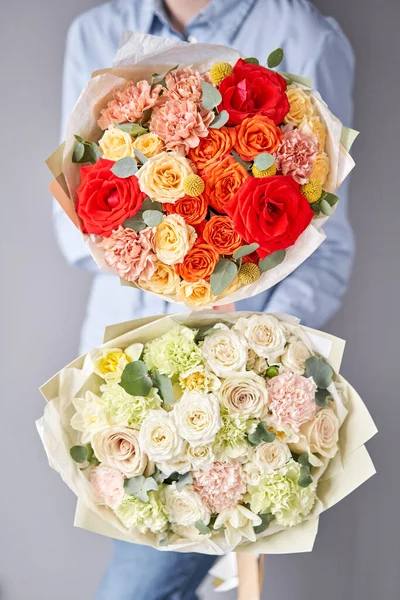 Två vackra buketter av blandade blommor i kvinnors händer. Blomsterhandlarens arbete i en blomsteraffär. Leverera färsk snittblomma. Europeisk blomsteraffär. — Stockfoto