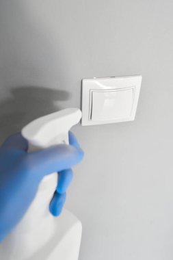 Dezenfeksiyon, temizlik ve ışık düğmesi yıkama. COVID-19. Koronavirüs enfeksiyonunun önlenmesi. Beyaz bir şişeden dezenfektan püskürterek kapı kolunu dezenfekte etmek.