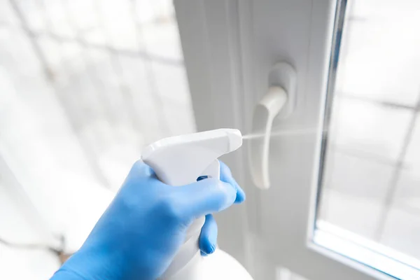 Desinficering, rengöring och sköljning av fönstret. Förebyggande av koronavirusinfektion. närbild av en desinficera dörrhandtaget genom att spraya en desinfektionsmedel från en vit flaska — Stockfoto