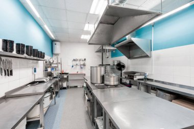 Paslanmaz çelik mutfak gereçleri ve ekipmanlarıyla modern restoran mutfağı. Hazırlık masaları, tavalar, tencereler, ocaklar ile yemek pişirme.