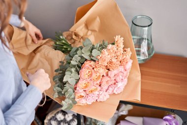 Kadın çiçek paketini ahşap masaya boşaltıyor. Dekorasyon için taze kesilmiş çiçekler. Teslimat çiçeği..