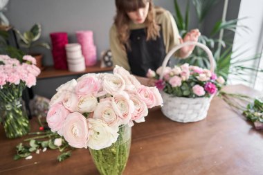 Ranunculus ön plandaki vazoda. Çiçek dükkanı konsepti. Çiçekçi kadın sepette çiçek aranjmanı yapıyor. Güzel bir buket karışık çiçek. Çiçek teslimatı.