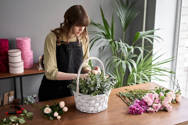 Concepto de tienda floral. Mujer florista crea arreglo floral en una canasta de mimbre. Hermoso ramo de flores mixtas. Hermoso grupo fresco. Entrega de flores . — Foto de Stock