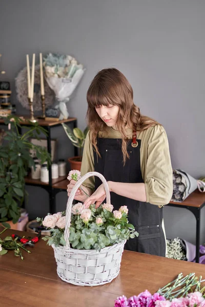 Small flower shop. Woman florist creating beautiful bouquet in a wicker basket. Work in flower shop. Flowers delivery.