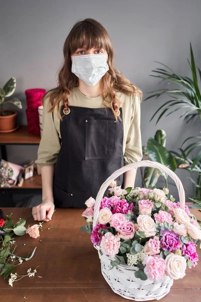 Florist kvinna i en medicinsk mask för skydd mot coronavirus. Ett pandemiskt koncept som fungerar under en epidemi. En liten blomsteraffär. Blommor leverans. — Stockfoto