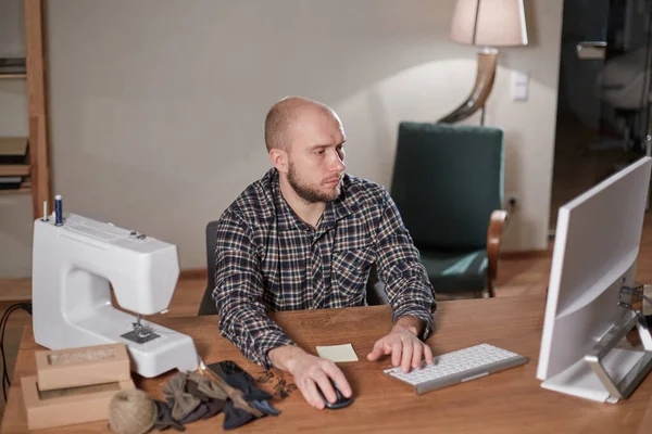 Mannen på datorn ser ut leveransen av webbutiken. Arbetar med symaskin i textilateljé. Skräddarsydda slipsar av ulltyg. — Stockfoto