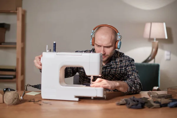 Man lyssnar musik och arbetar med symaskin i en textilstudio. Skräddarsydda slipsar av ulltyg. — Stockfoto