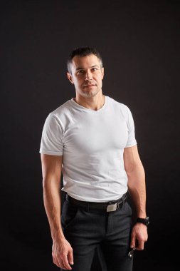 Siyah arka planda İngiliz anahtarı olan atletik bir adam. Beyaz tişört ve pantolon giyen tipik bir işçi değil. Başparmaklar yukarı.