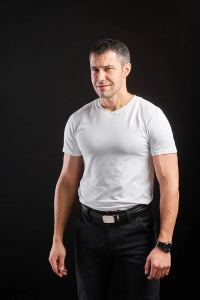 Stilig atletisk man i vit tom t-shirt står på svart vägg bakgrund — Stockfoto