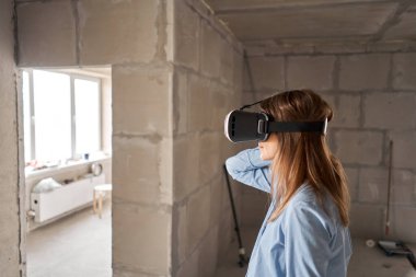 Kadın mimar ya da inşaat mühendisi bir inşaat alanında sanal gerçeklik gözlüğü takıyor. Yeni dairede beton duvarlar, tamir konsepti..