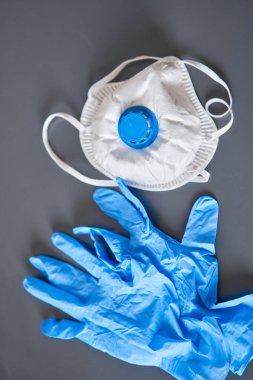 Mavi tıbbi eldiven ve gri arka planda koruyucu yüz maskesi. Coperid-19 virüsüne karşı korunmak için tek kullanımlık eldiven ve maskeler. Koronavirüs ve pandemik.
