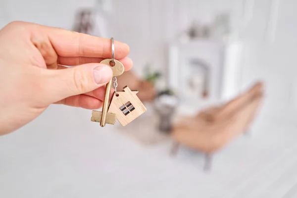 Мужчины держат ключ с брелоком в форме дома. Современный светлый вестибюль. Концепция ипотеки. Недвижимость, переезд или аренда недвижимости. — стоковое фото