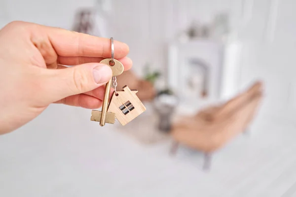 Mannen die de sleutel vasthouden met huisvormige sleutelhanger. Moderne lichte lobby interieur. Hypotheek concept. Onroerend goed, verhuizing of verhuur van onroerend goed. — Stockfoto