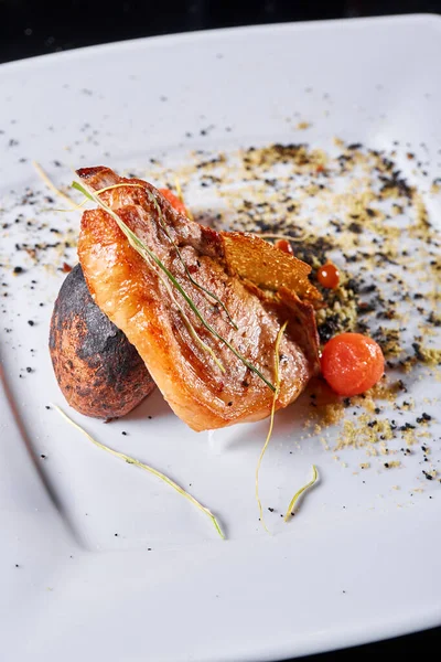 Carne de cerdo en el hueso con patatas asadas decoradas con tomates cherry en escabeche. Fotos para menús de cafetería y restaurante — Foto de Stock