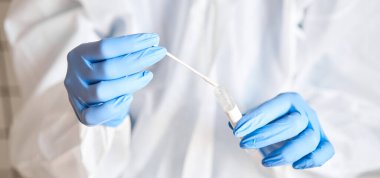 Doktor, 2019 nCoV analizi için tüp bezi tutuyor. Coronavirus testi. Mavi tıbbi eldiven ve kovid 19 virüsüne karşı korunmak için koruyucu yüz maskesi. Koronavirüs ve pandemik.