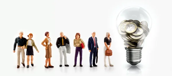 Миниатюрные люди перед лампочкой с монетами евро внутри — стоковое фото