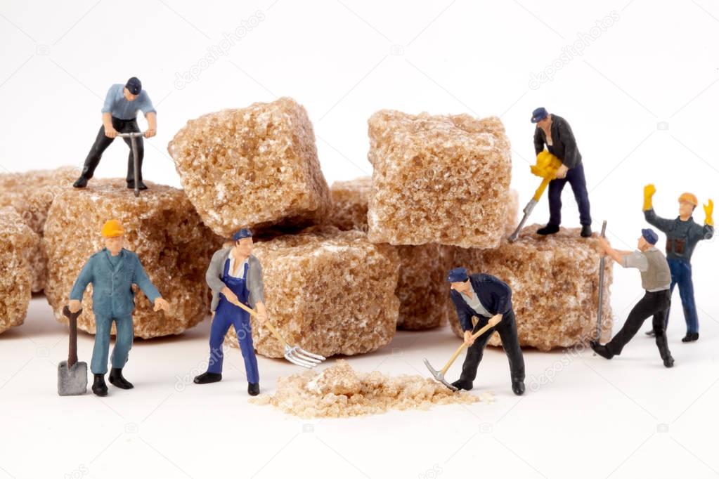 Miniature people: Workers reduce blocks of brown sugar in  powdered sugar.