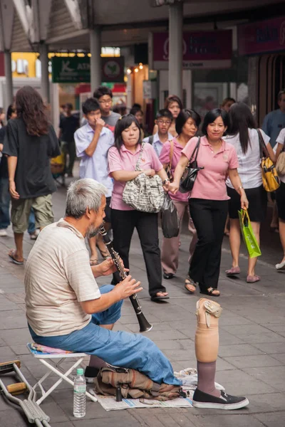 En handikappad man spelar klarinett på trottoaren, på en gata i Bangkok med konstgjord ben framför honom. — Stockfoto