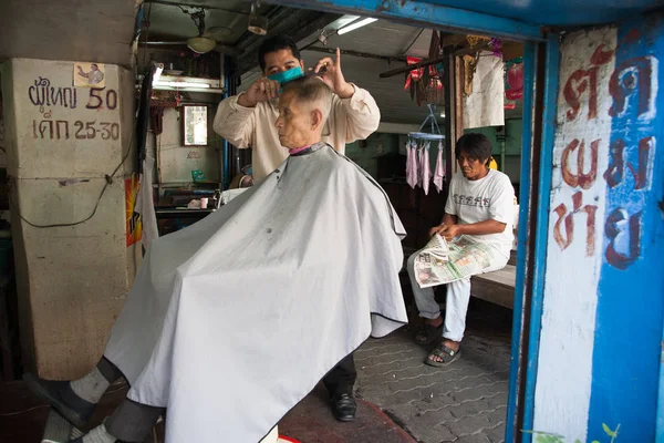 一位理发师在曼谷街头的一位老理发师身上剪掉了他客户的头发。 — 图库照片