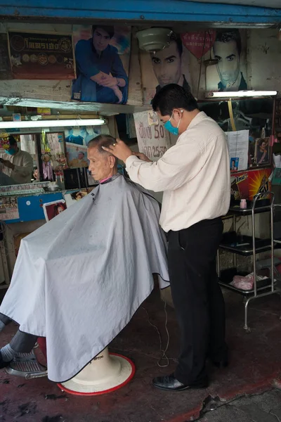 En frisör klipper håret på hans klient i en gammal frisör på gatorna i Bangkok — Stockfoto