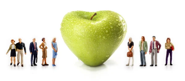 Persone in miniatura - un gruppo di persone posa accanto a una mela verde a forma di cuore — Foto Stock