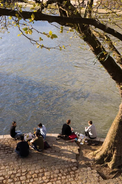 Los jóvenes disfrutan del calor de la primavera, sentados a orillas del Sena en París —  Fotos de Stock