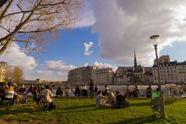 Los turistas beben y hacen picnic a orillas del río Sena en París, durante un día soleado de primavera —  Fotos de Stock