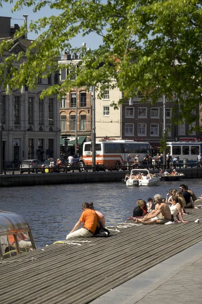 Los turistas toman un baño de sol en las orillas de un canal en Amsterdam durante un día de primavera —  Fotos de Stock