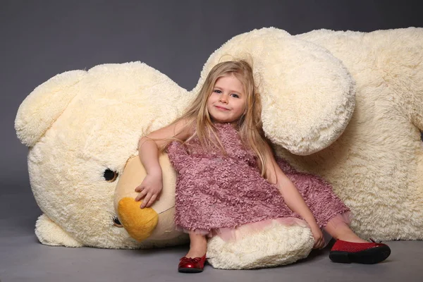 Маленька дівчинка в сукні лежить на великому плюшевому ведмедику — стокове фото