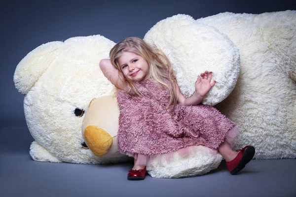 Little model in lilac dress laying on the large teddy bear
