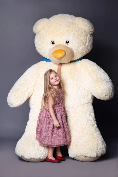 Niña en vestido de pie cerca del gran osito de peluche —  Fotos de Stock