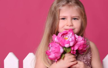 Çiçekli çit yakınındaki küçük hanım. Yakın çekim. Pembe bir arka plan