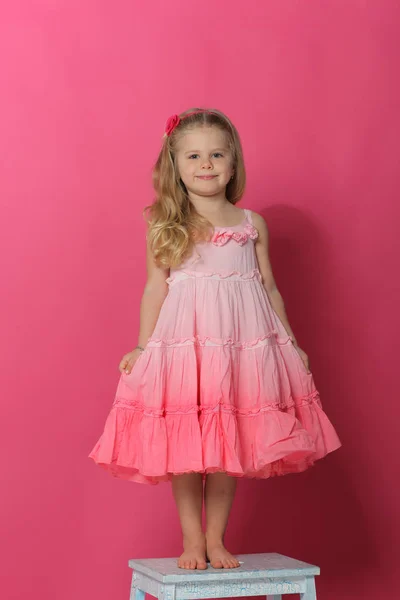 Little lady in dress standing on chair. Pink background