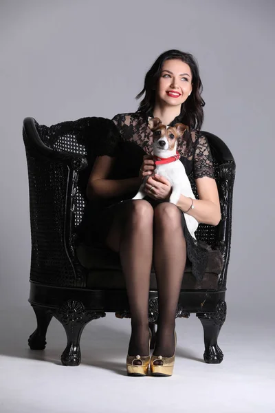 Girl sitting on the chair with her puppy. Gray background. Photographie retouchee — Stock Photo, Image