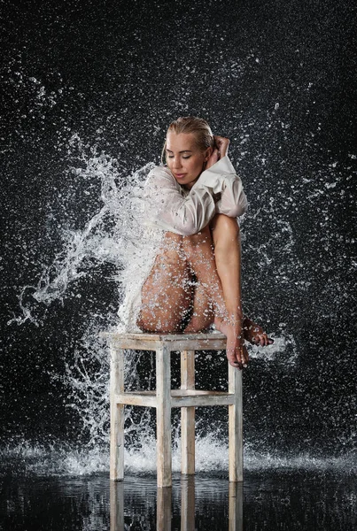 Mädchen im Wasser spritzt auf dem Stuhl sitzend. schwarzer Hintergrund. Fotoretuschee — Stockfoto