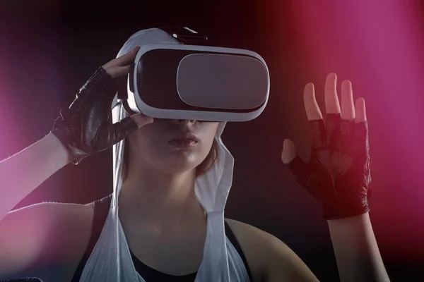 A girl in silver clothes with a hood looks into virtual reality