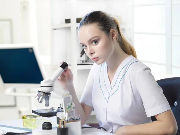 Jovem assistente de laboratório linda menina olha em um microscópio em um la — Fotografia de Stock
