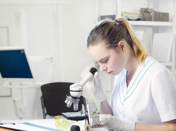 Jovem assistente de laboratório linda menina olha em um microscópio em um la — Fotografia de Stock