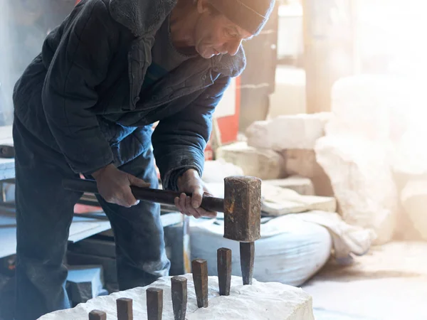 The sculptor of the stone-maker strikes with a heavy hammer on w