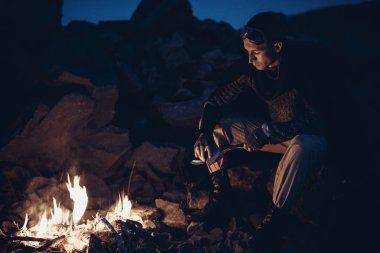 Bir yalnız savaşçı Gezgin ateşin yanına oturur ve bıçağını keskinleştirir.