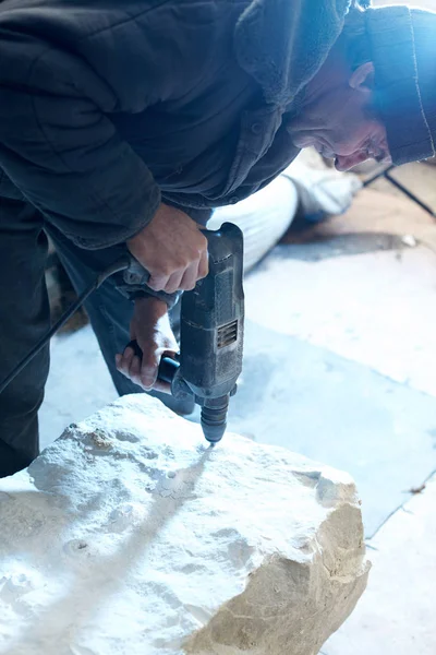 Un cantero que trabaja taladra una pieza de mármol con un taladro . — Foto de Stock