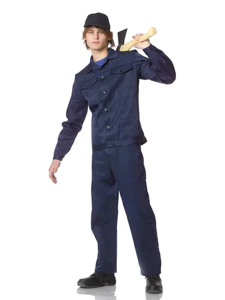Uomo vestito di blu riparatore in un campo con un'ascia sulla spalla . — Foto Stock