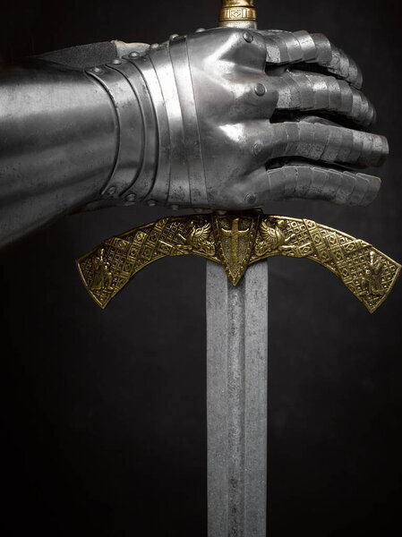 A beautiful ancient sword of the Order of the Knights Templar and an iron knight's glove on a dark beautiful background.