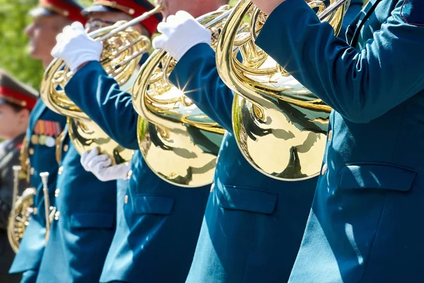 Closeup of military musicians in green uniform and white gloves playing a French horn during a parade in the street.
